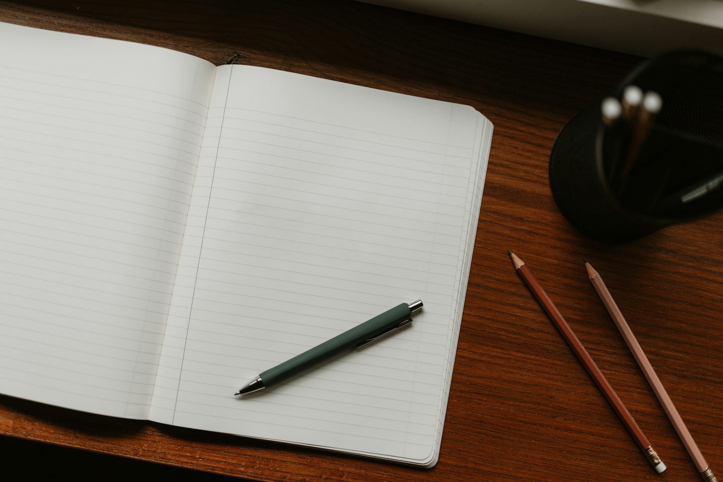 An open notebook with pens and pencils on a desk